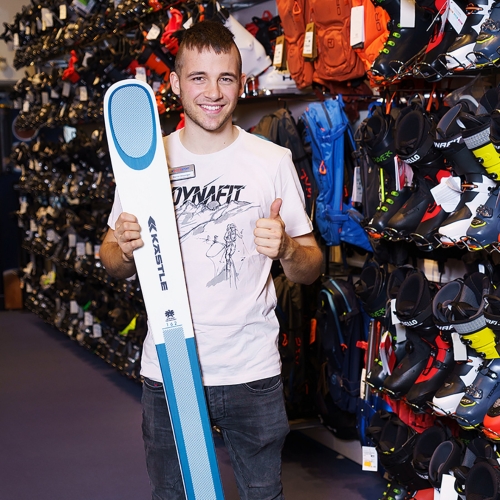 Mann hält KÄSTLE Ski in einem Skigeschäft, trägt ein Dynafit Shirt und ist von Skischuhen und Ausrüstung umgeben.