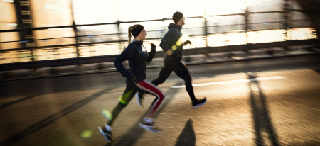 Paar läuft bei Sonnenuntergang im Freien auf einer Brücke; Fitness-Training und Konzept für einen gesunden Lebensstil.