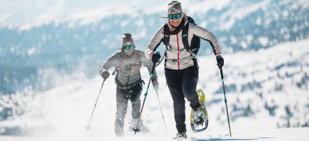 Zwei Personen gehen mit Schneeschuhen in einer verschneiten Berglandschaft und genießen die winterliche Freizeitaktivität im Freien.