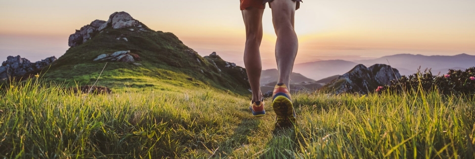 Beine und Schuhe eines Trailrunners auf einem grasbewachsenen Bergpfad bei Sonnenuntergang. Outdoor-Fitness.