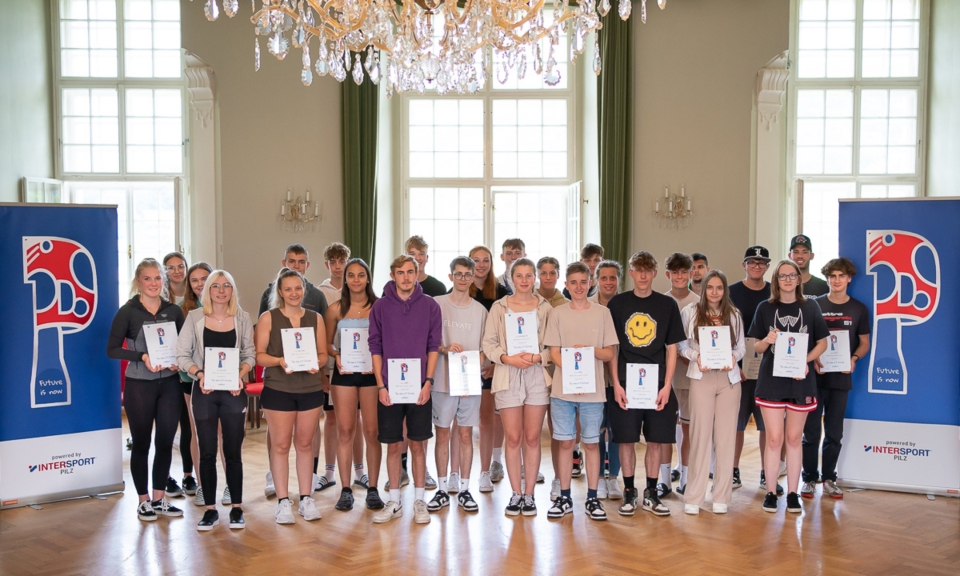 A group of students poses with certificates in a lavish hall, graduation ceremony with sponsor banners.