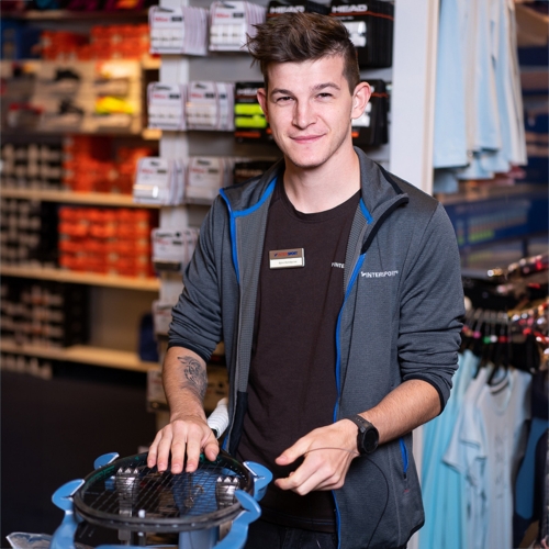 Mitarbeiter eines Sportartikelgeschäfts mit Tennisschläger im Einzelhandel. Sportausrüstung verfügbar.