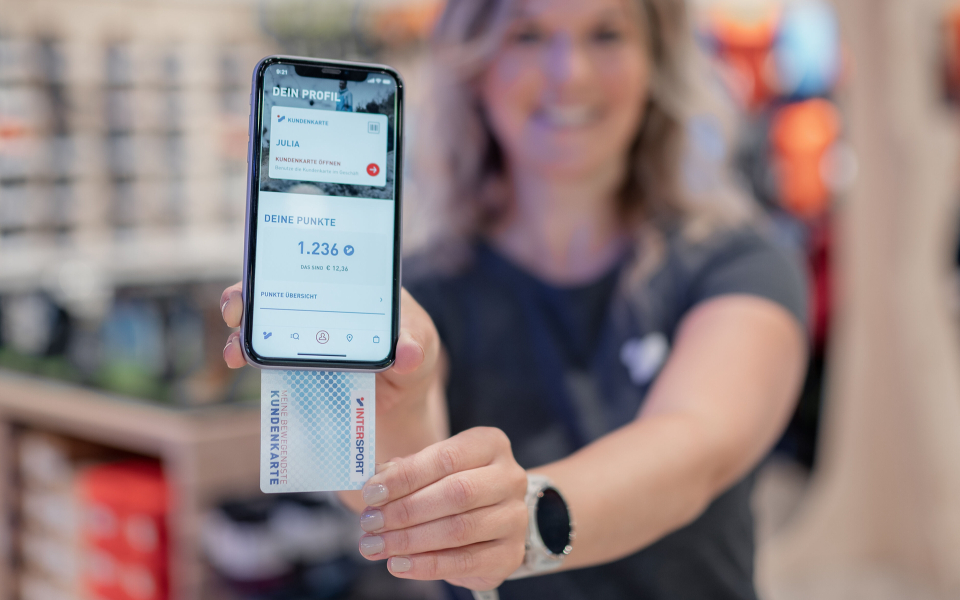 Frau hält Smartphone mit Sport-App und Kundenkarte im Geschäft.