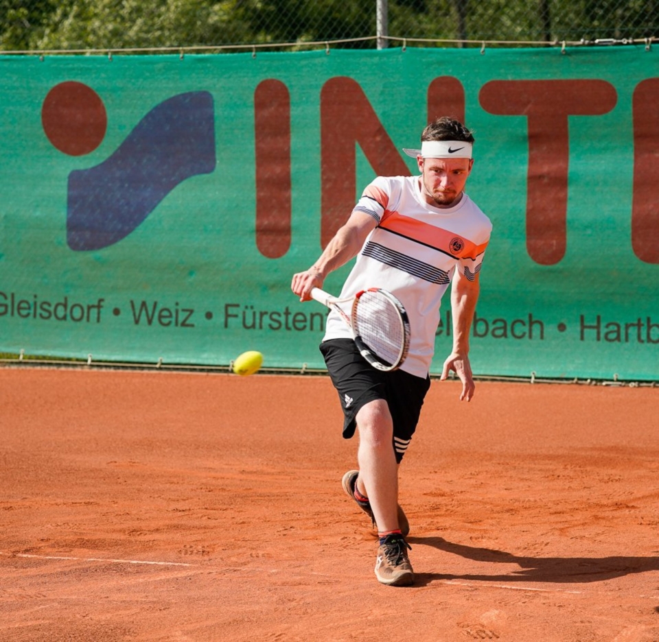 Tennisspieler schlägt eine Vorhand auf einem Sandplatz vor einer Sponsorenbande.