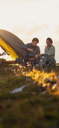 Couple camping: Man pours water near tent at sunset. Outdoor adventure travel.