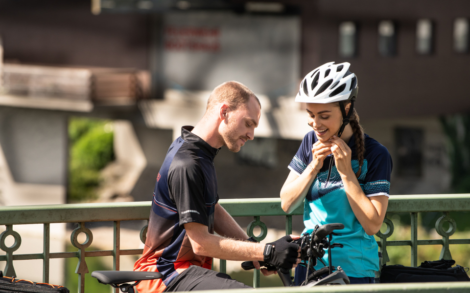 Ein Paar bereitet sich auf eine Fahrradtour vor: Die Frau justiert ihren Helm, der Mann überprüft die Fahrradausrüstung. Outdoor-Fahrradabenteuer.