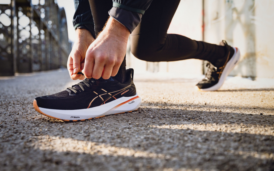 Läufer bindet Schnürsenkel an Asics Laufschuhen im Freien vor einem Lauf auf einer Stadtbrücke.