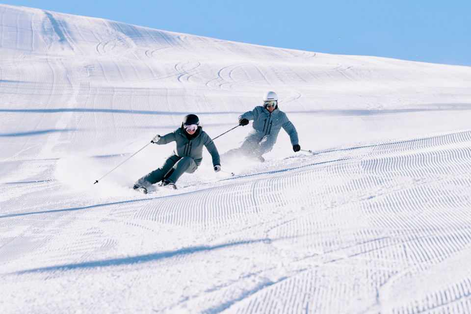 Zwei Skifahrer in Aktion auf einer präparierten Skipiste, die den Wintersport in den Bergen genießen.