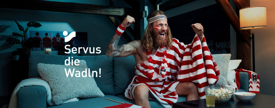 Frau, die in einem Park läuft und ein geblümtes Kleid trägt, mit dem Text "Servus die Wadln!" als Overlay.