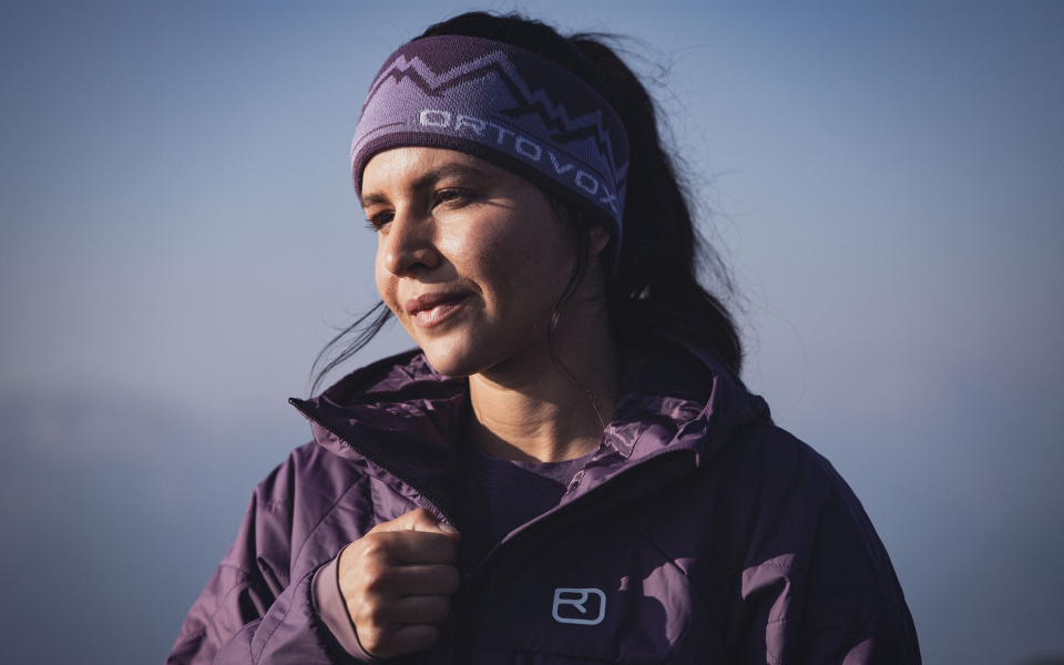 Frau mit Ortovox-Stirnband und violetter Jacke im Freien zum Wandern oder für Wintersport.