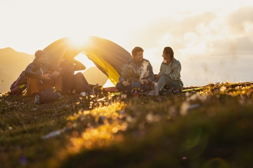 Camper entspannen im Sonnenuntergang vor ihrem Zelt in den Bergen; Outdoor-Abenteuerreise-Lifestyle.