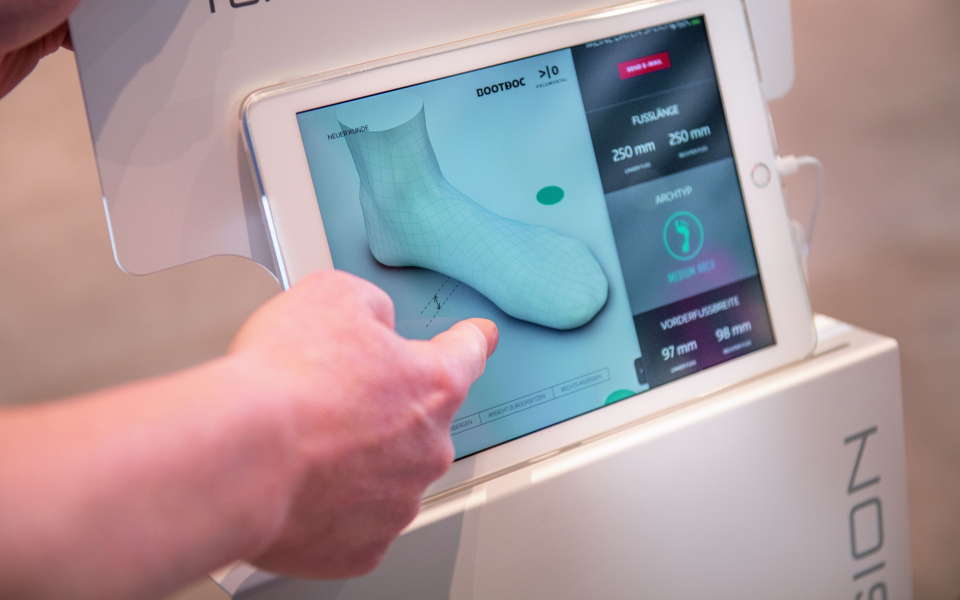 Fußscanner-Technologie: Hand interagiert mit einem Tablet, das ein 3D-Fußmodell für individuelle Orthopädieeinlagen anzeigt.
