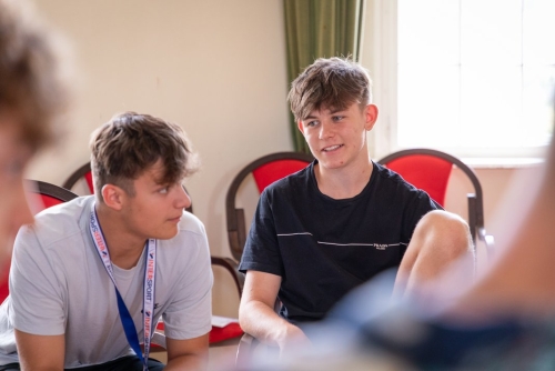 Zwei jugendliche Jungen sitzen in roten Stühlen auf einer Jugendkonferenz und diskutieren.