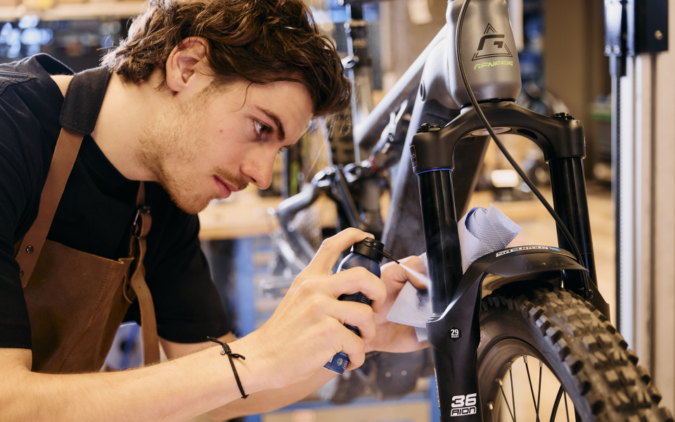 Ein Fahrradmechaniker reinigt eine Vorderradgabel mit Sprühreiniger in einer Fahrradwerkstatt.