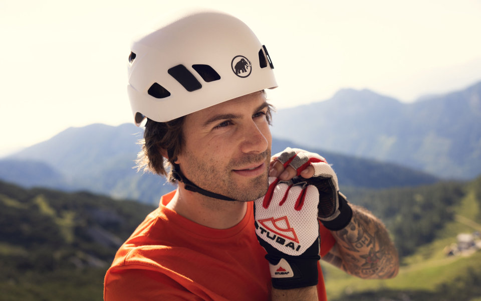 Mann mit Kletterhelm und Handschuhen vor Bergpanorama. Outdoor-Ausrüstung für Abenteuer.