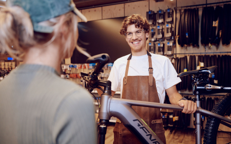 Lächelnder Fahrradmechaniker in einem Fahrradladen hilft einem Kunden beim Kauf eines neuen Fahrrads. Fahrradreifen im Hintergrund.