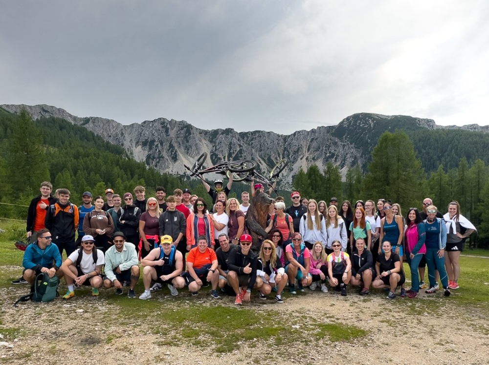 Großes Gruppenfoto: Wanderer posieren in der Nähe einer Berglandschaft mit Holzskulptur, Outdoor-Abenteuerreisen.