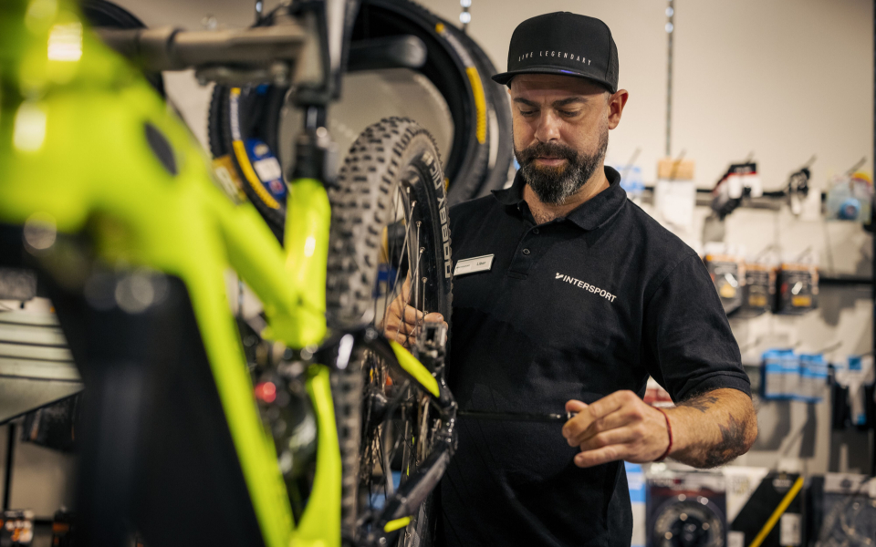 Ein Fahrradmechaniker repariert ein Mountainbike in einem Fahrradladen, wobei er sich auf das Hinterrad konzentriert.