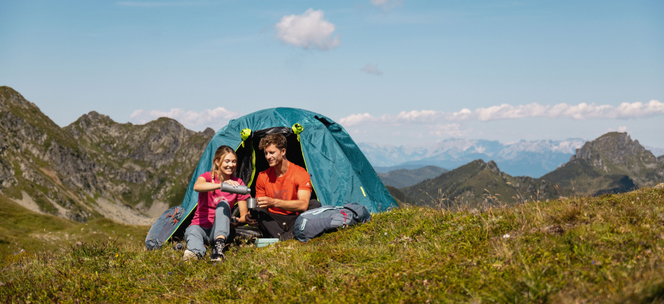 Paar campt mit blauem Zelt in den Bergen. Outdoor-Abenteuer und Wander-Lifestyle.