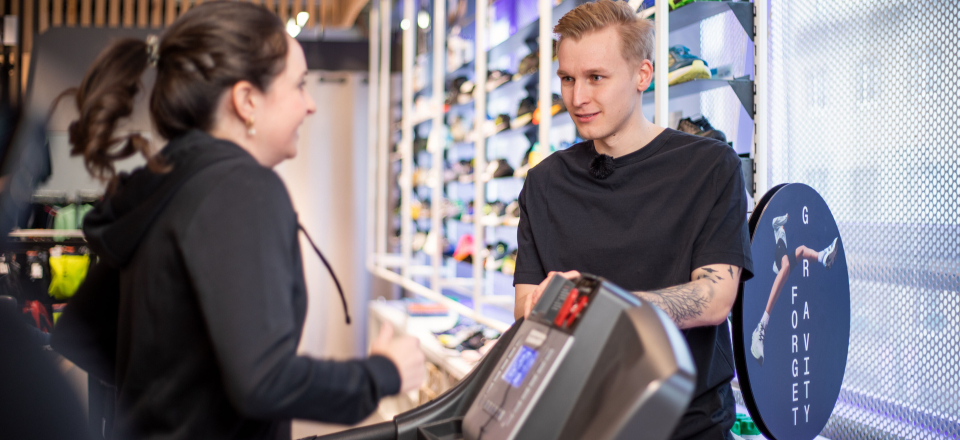 Frau auf einem Laufband, die von einem Fitnesstrainer in einem modernen Fitnessstudio unterstützt wird.