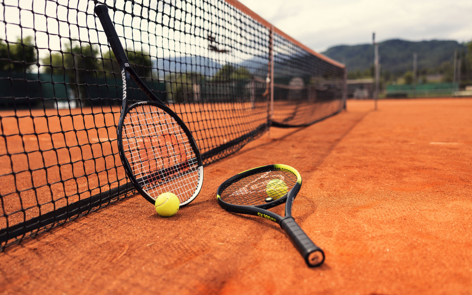 Tennisschläger und -bälle auf einem Sandplatz mit Netz, bereit für ein Match. Sport und Freizeit.