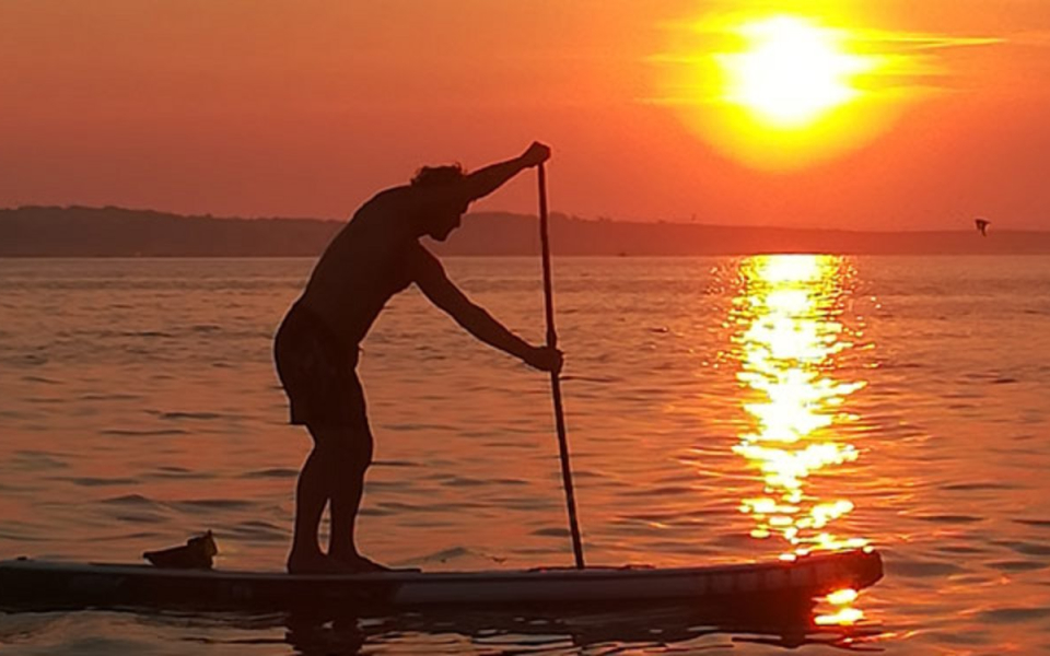Frau beim Paddeln auf ruhigem Wasser bei Sonnenuntergang; Stand-up-Paddle-Board-Yoga und Fitness.