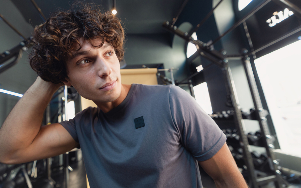 Junger Mann mit lockigem Haar in grauem Sportshirt in einem modernen Fitnessstudio; Fitness-Lifestyle.