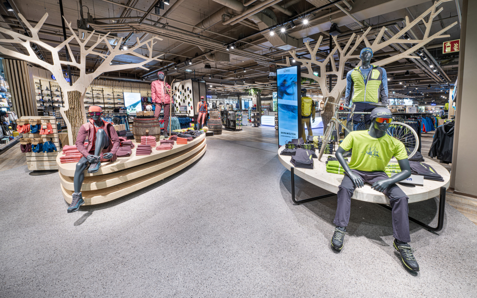 Innenraum eines Outdoor-Bekleidungsgeschäfts mit Schaufensterpuppen, die Wander- und Abenteuerausrüstung präsentieren.