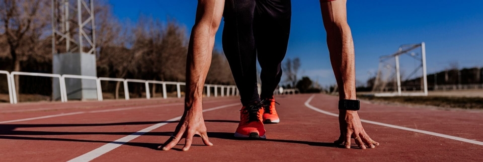 Läufer in Startposition auf roter Bahn bereit für Sprintrennen, Fitness- und Leichtathletikkonzept.