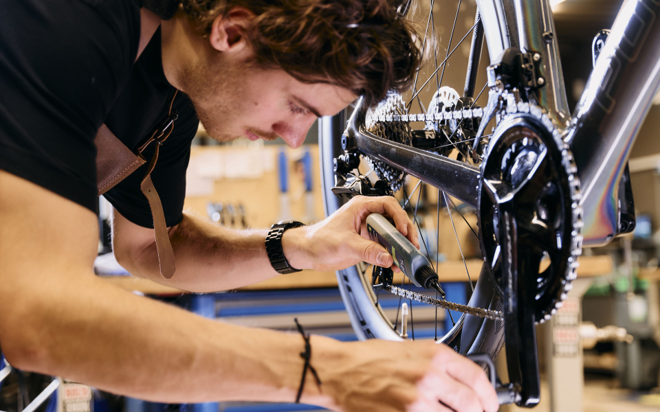 Fahrradmechaniker repariert Fahrradkette mit Schmiermittel in der Werkstatt für Fahrradwartung.