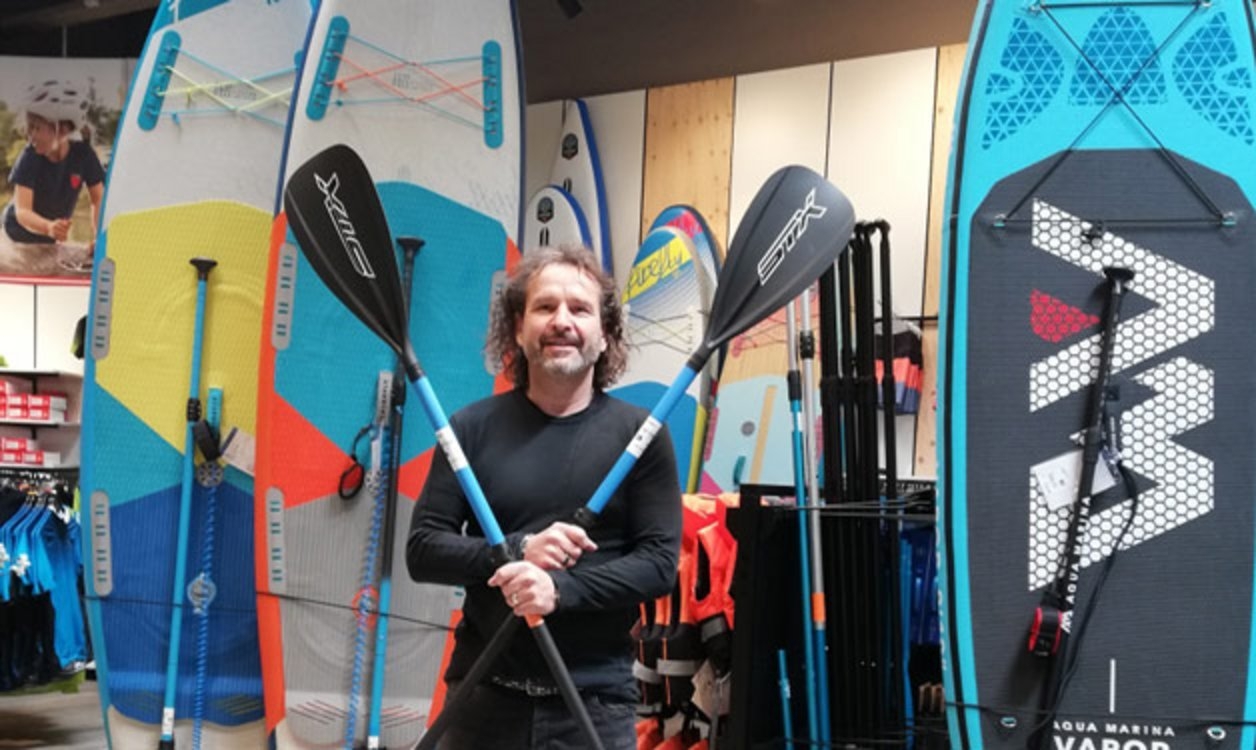 Mann mit Paddel in einem Surfshop mit Stand-Up-Paddle-Boards zum Verkauf.