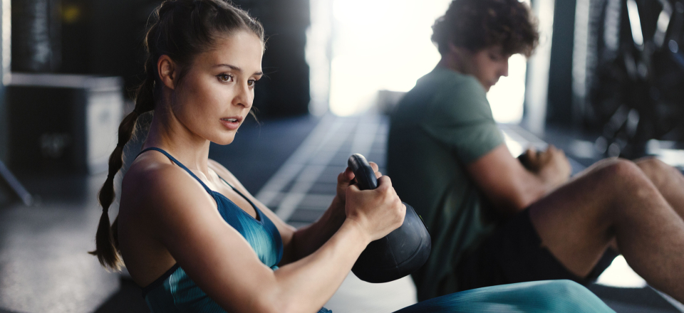 Frau und Mann machen Russian Twists mit Kettlebells während eines Core-Workouts im Fitnessstudio.