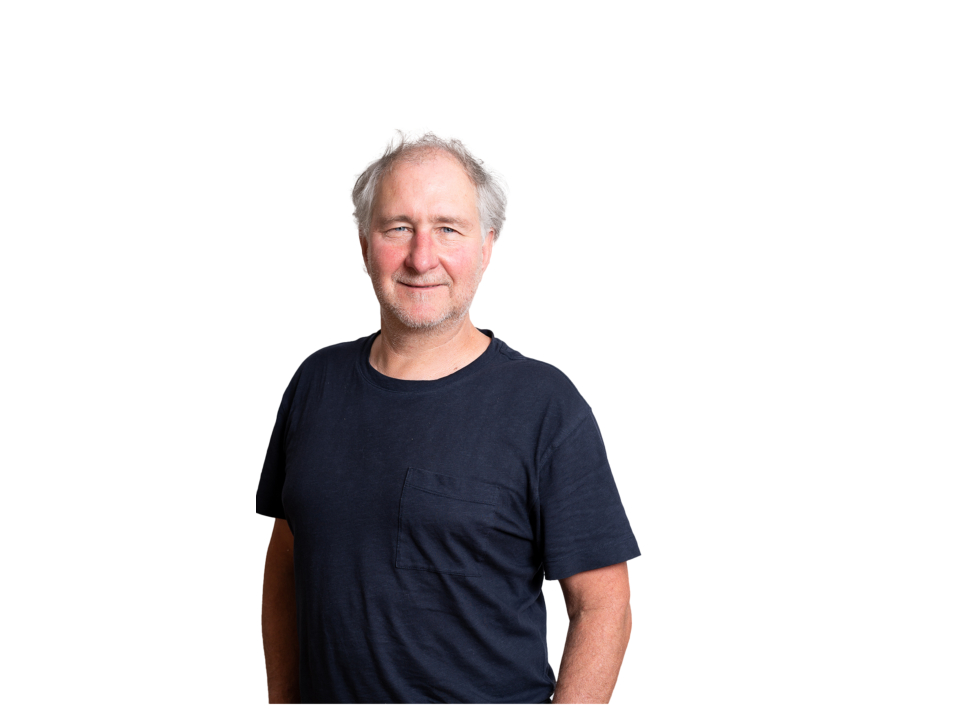 Porträt eines reifen Mannes mit ergrauendem Haar, der ein marineblaues T-Shirt vor einem weißen Hintergrund trägt.