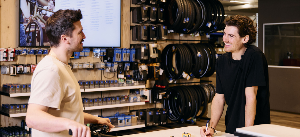 Ein Mann kauft ein neues Mountainbike in einem lokalen Fahrradgeschäft; ein Verkäufer hilft beim Kauf.