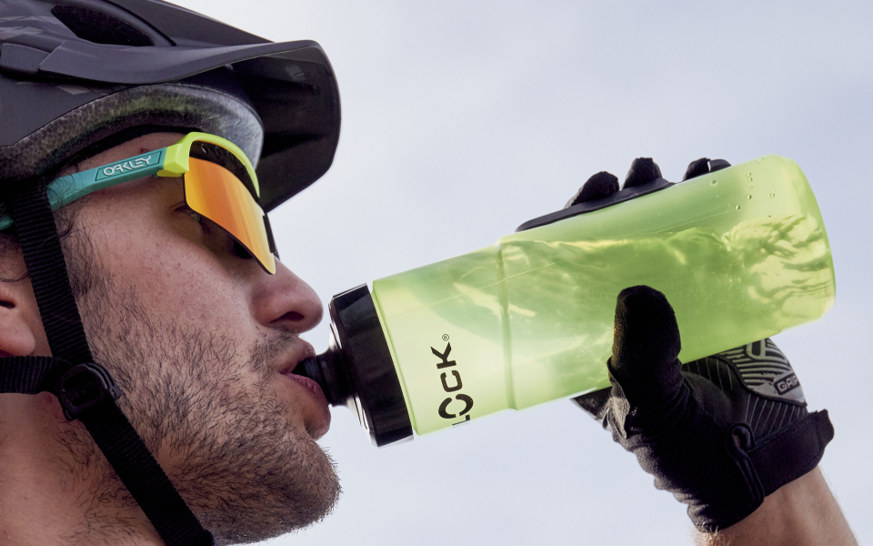 Mountainbiker trinkt aus einer grünen Wasserflasche; Flüssigkeitszufuhr beim Radfahren im Freien.