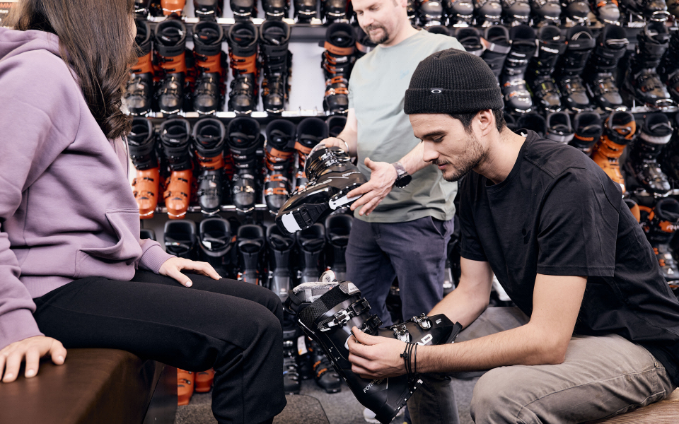 Ein Mann passt einem Kunden Skischuhe in einem Skigeschäft an, in dem Reihen von Skischuhen zum Verkauf stehen.