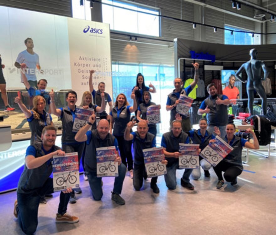 Eine Gruppe von Asics-Einzelhandelsmitarbeitern feiert eine Fahrradaktion mit Postern im Geschäft.