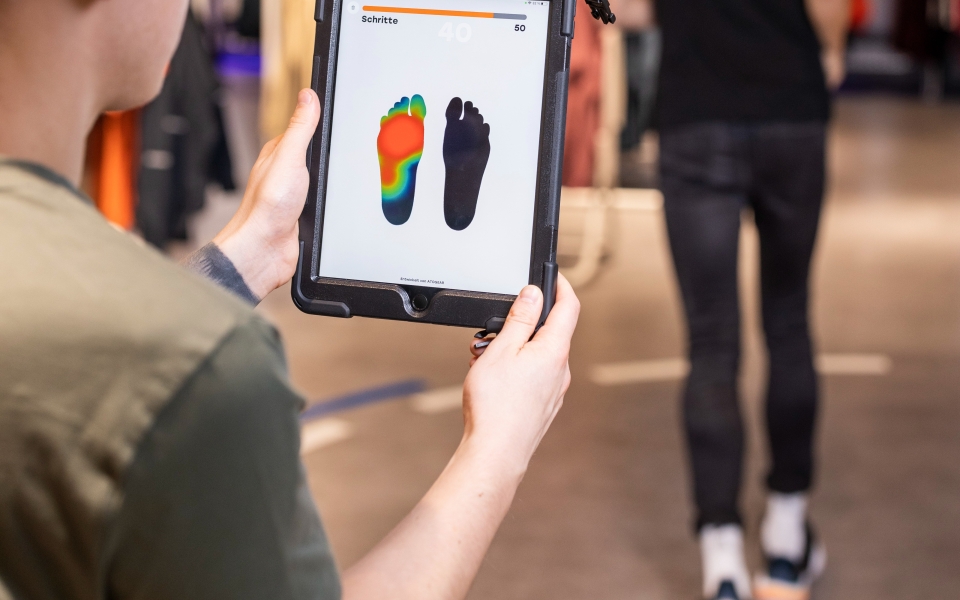 Fußscan auf einem Tablet, der Druckpunkte für die Anpassung von individuellen orthopädischen Einlagen in einem Schuhgeschäft anzeigt.