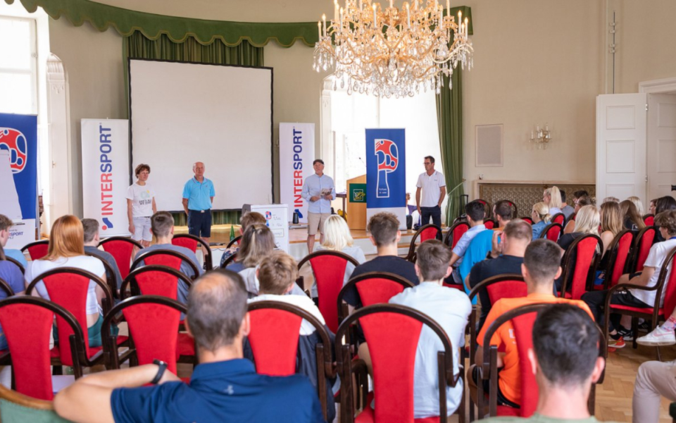 Intersport-Präsentation: Redner wenden sich in einem prunkvollen Saal mit roten Stühlen und Kronleuchter an das Publikum.